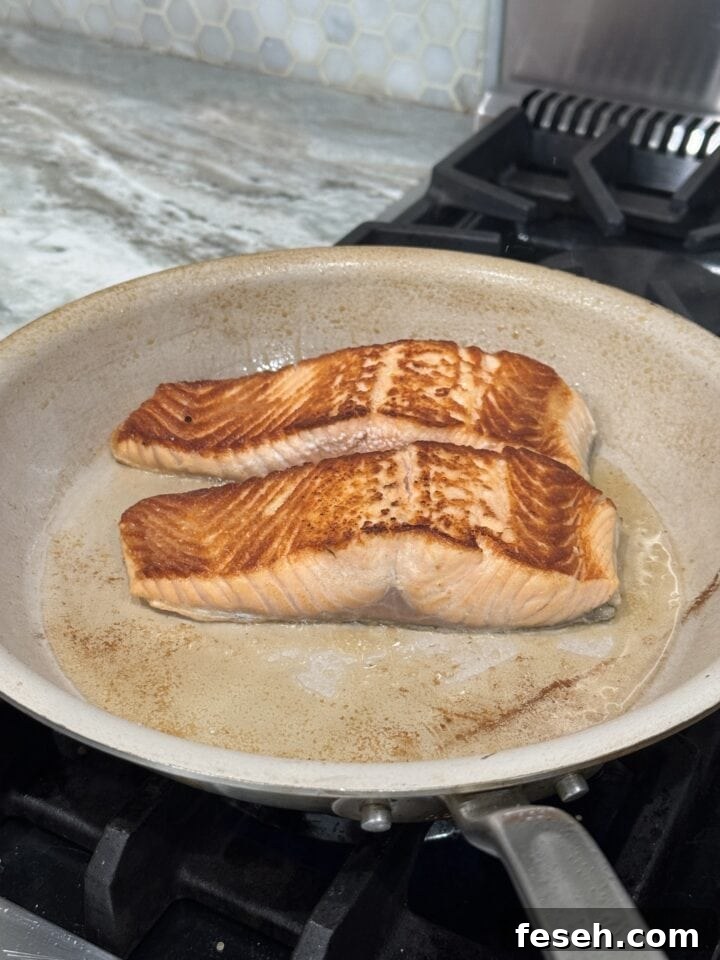 a photo of two pieces of salmon in a nonstick pan on the stove