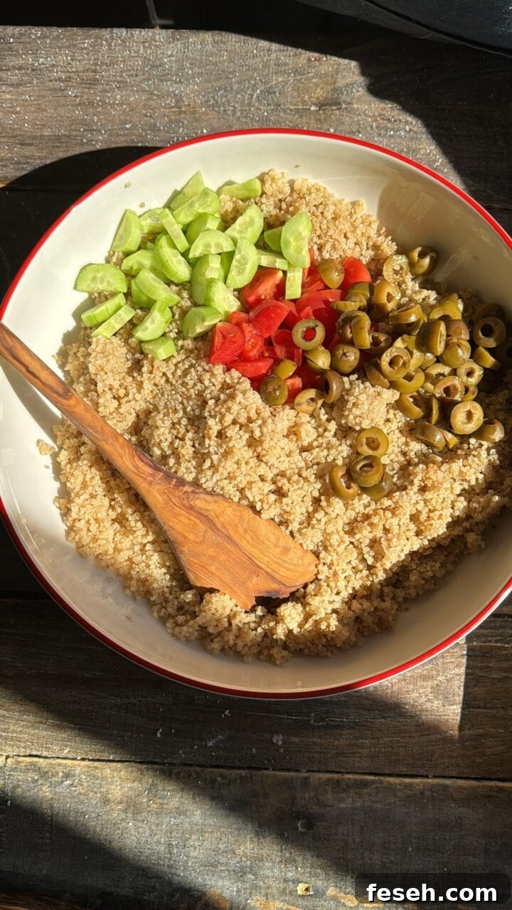 a photo of quinoa, olives, tomatoes and cucumbers in a bowl with a wooden spoon