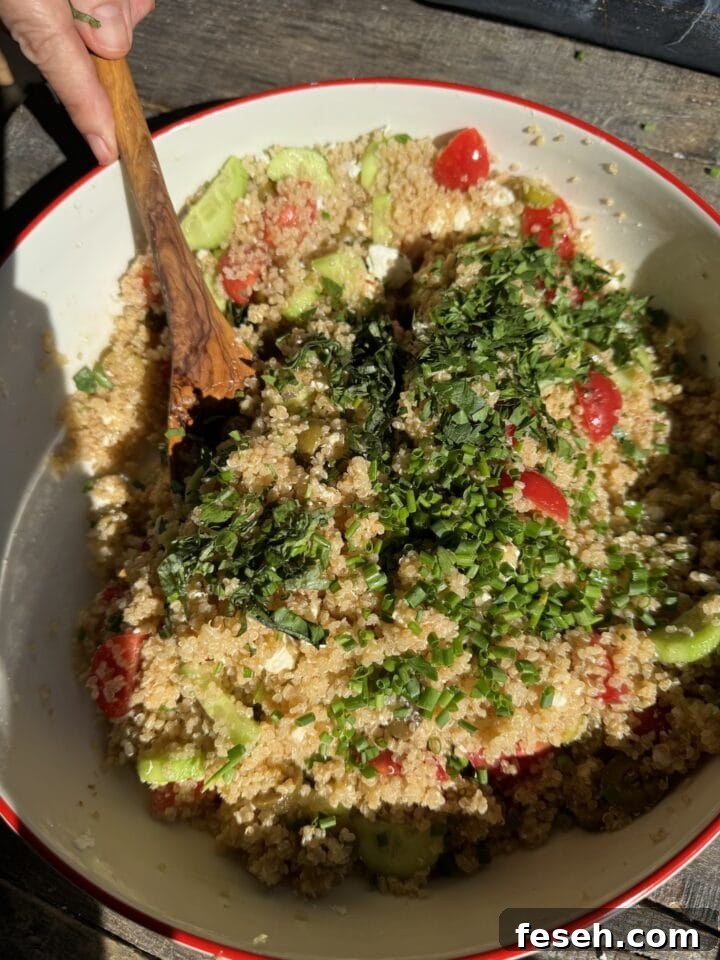 a photo of herbs added on top of the quinoa salad in a white bowl with a wooden spoon