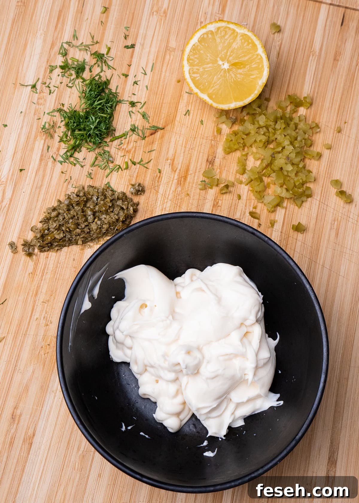Mayonnaise in a bowl, chopped capers,Gerkin, dill and half a lemon on a wooden chopping board