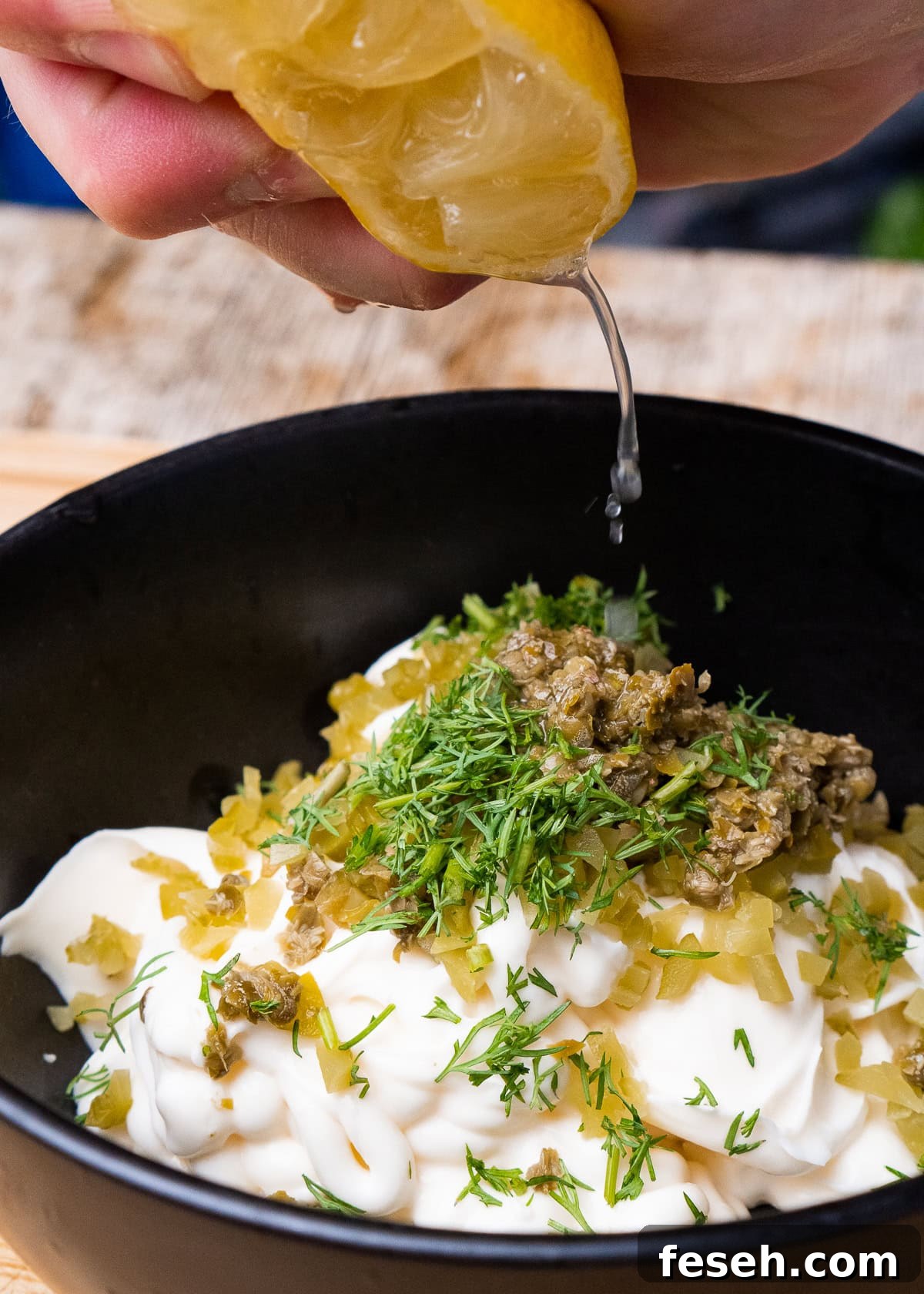 Mayonnaise, chopped capers, Gerkin and dill in a bowl with lemon juice being squeezed over the top