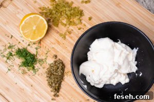 Mayonnaise in a bowl, chopped capers,Gerkin, dill and half a lemon on a wooden chopping board