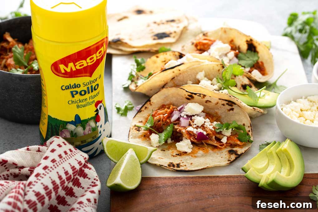 Shredded Chicken Tinga tacos and all the fixings on a white surface.