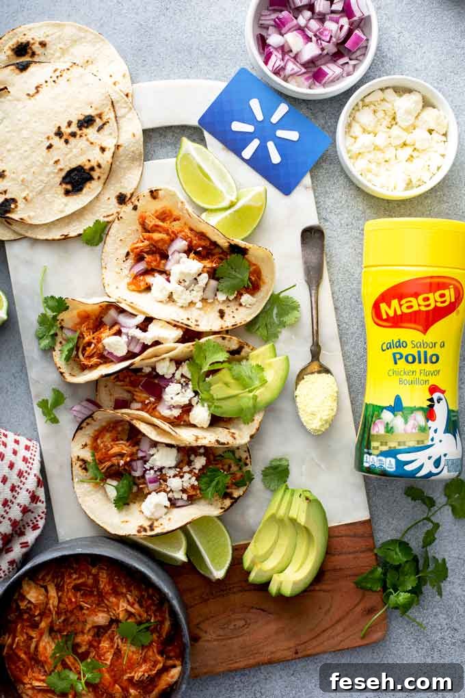 Shredded Chicken Tinga tacos and all the fixings on a white surface.