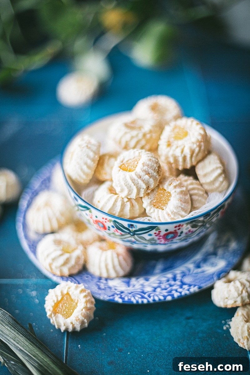 A colorful bowl filled with Butter Cookies with Pandan that sits on a blue and white plate with more Butter Cookies