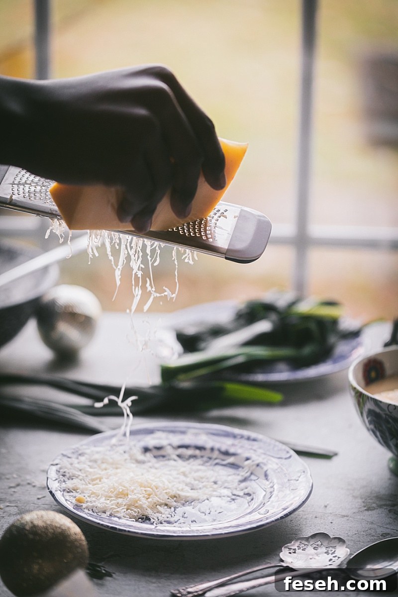 A boy's hand grating Gouda cheese on a hand grater over a blue and white decorative plate for Indonesian Butter Cookies with Pandan