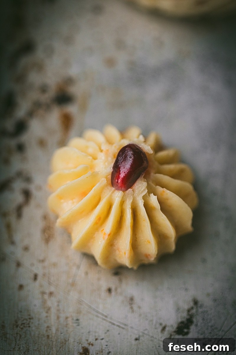 Close up shot of an Indonesian butter cookie dough that was piped onto a cookie sheet with a pomegranate seed placed in the middle