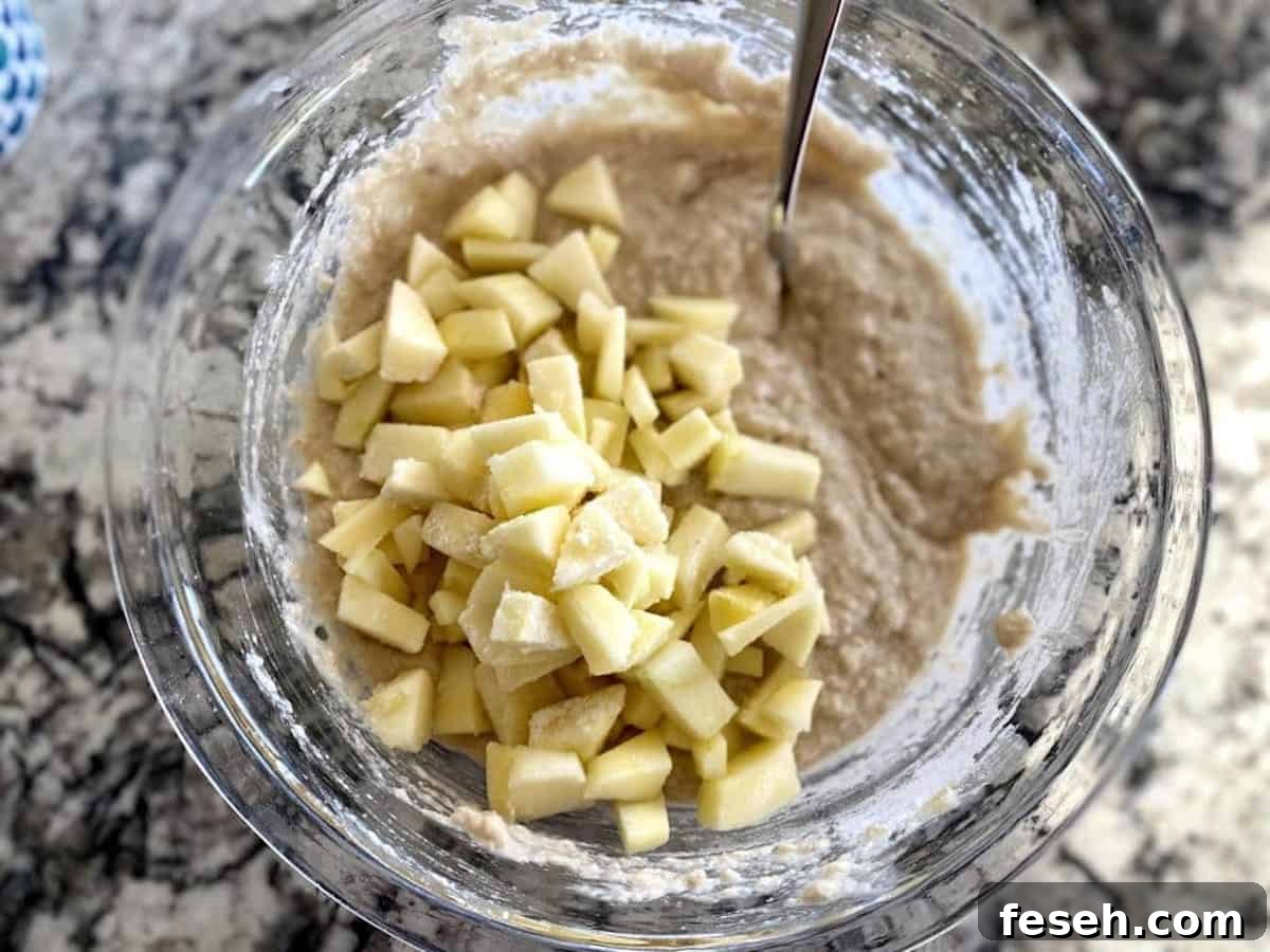 Adding cut, peeled apples to the bread batter in a bowl on the counter