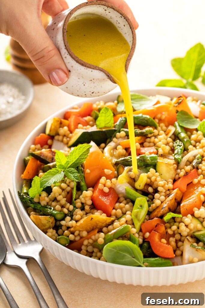 Israeli couscous and grilled vegetables salad getting drizzled with vinaigrette