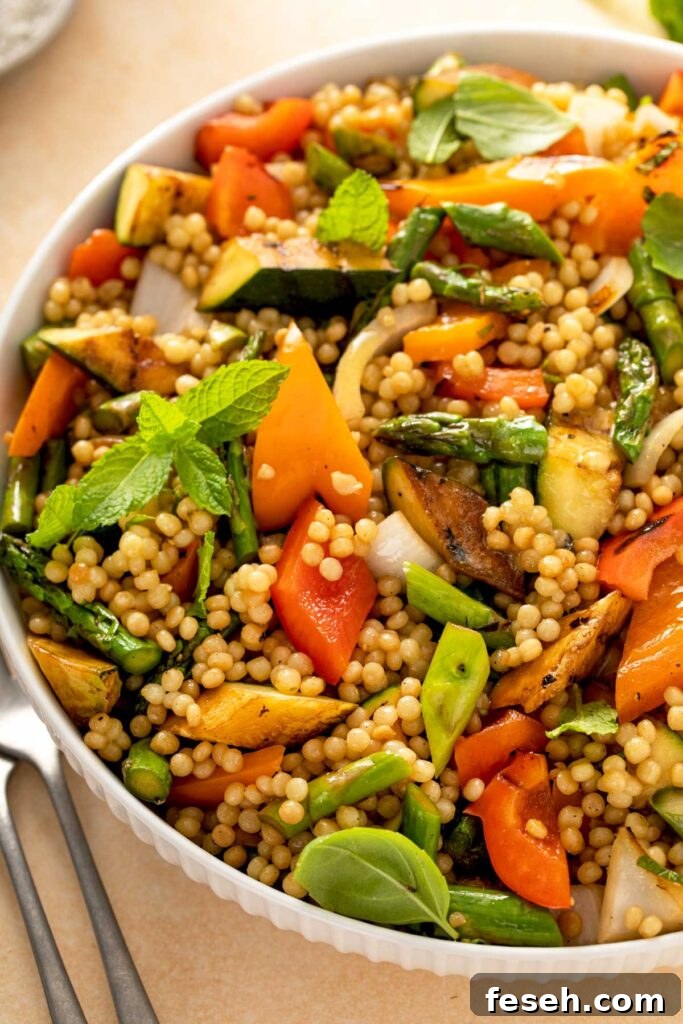 Close up view of a bowl filled with couscous pasta salad with grilled asparagus, bell peppers and summer squash