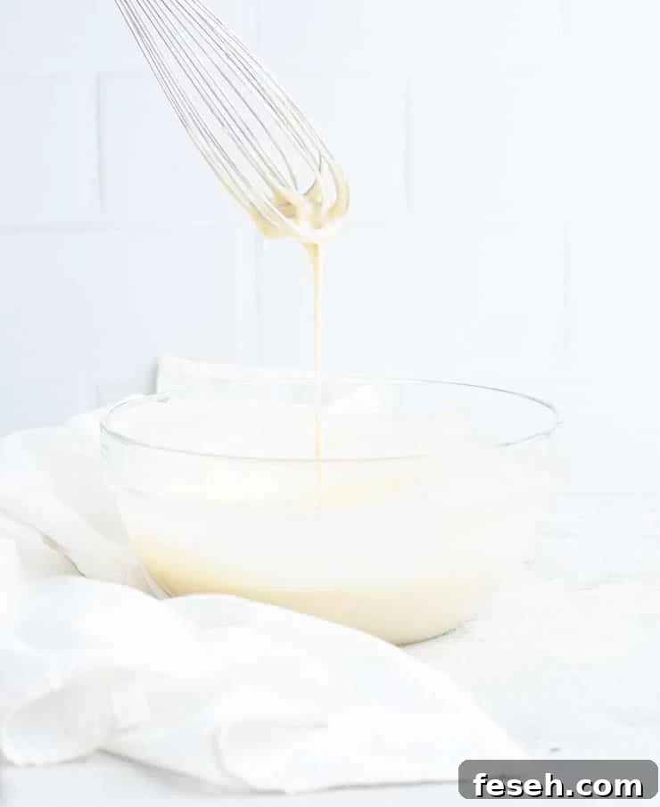 Rosette batter dripping off a whisk and into a clear bowl.
