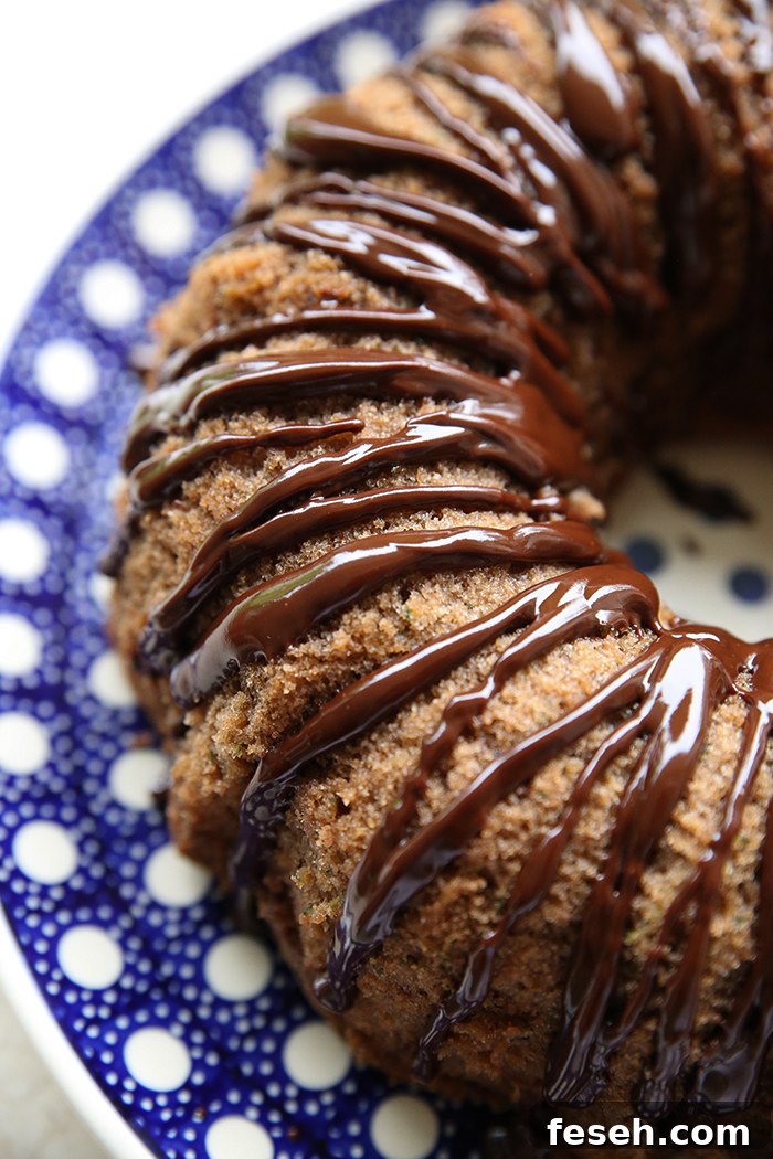 Half of a spiced chocolate zucchini bundt cake with chocolate ganache on a round dark blue and white polka-dotted Polish pottery plate.