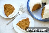 Two slices of pumpkin bundt cake with cream cheese frosting sitting on small plates with two forks crisscross on each other between the plates. In the upper right corner is a pumpkin bundt cake with cream cheese frosting on a round platter with a couple slices cut out.