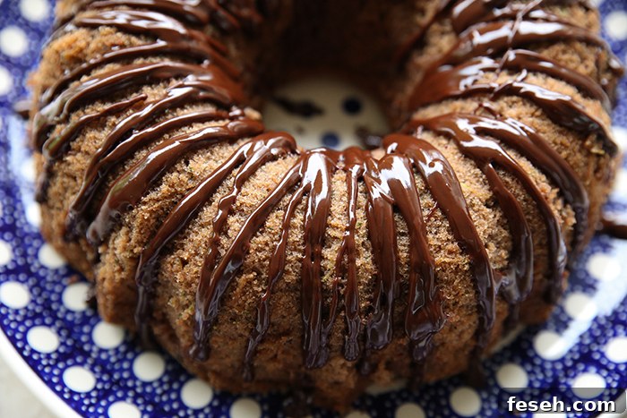 A closeup picture of a chocolate zucchini bundt cake drizzled with chocolate ganache sitting on a round dark blue Polish pottery plate with white polka dots.