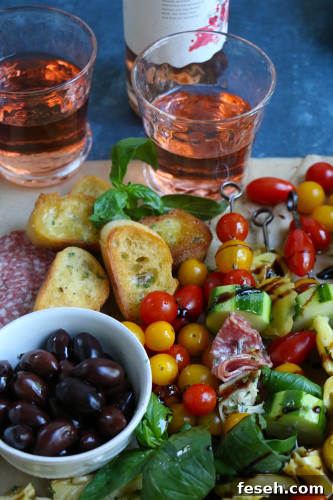 Summer Tortellini Pasta Salad on skewers, a bowl of olives, slices of bread, and two glasses of wine.