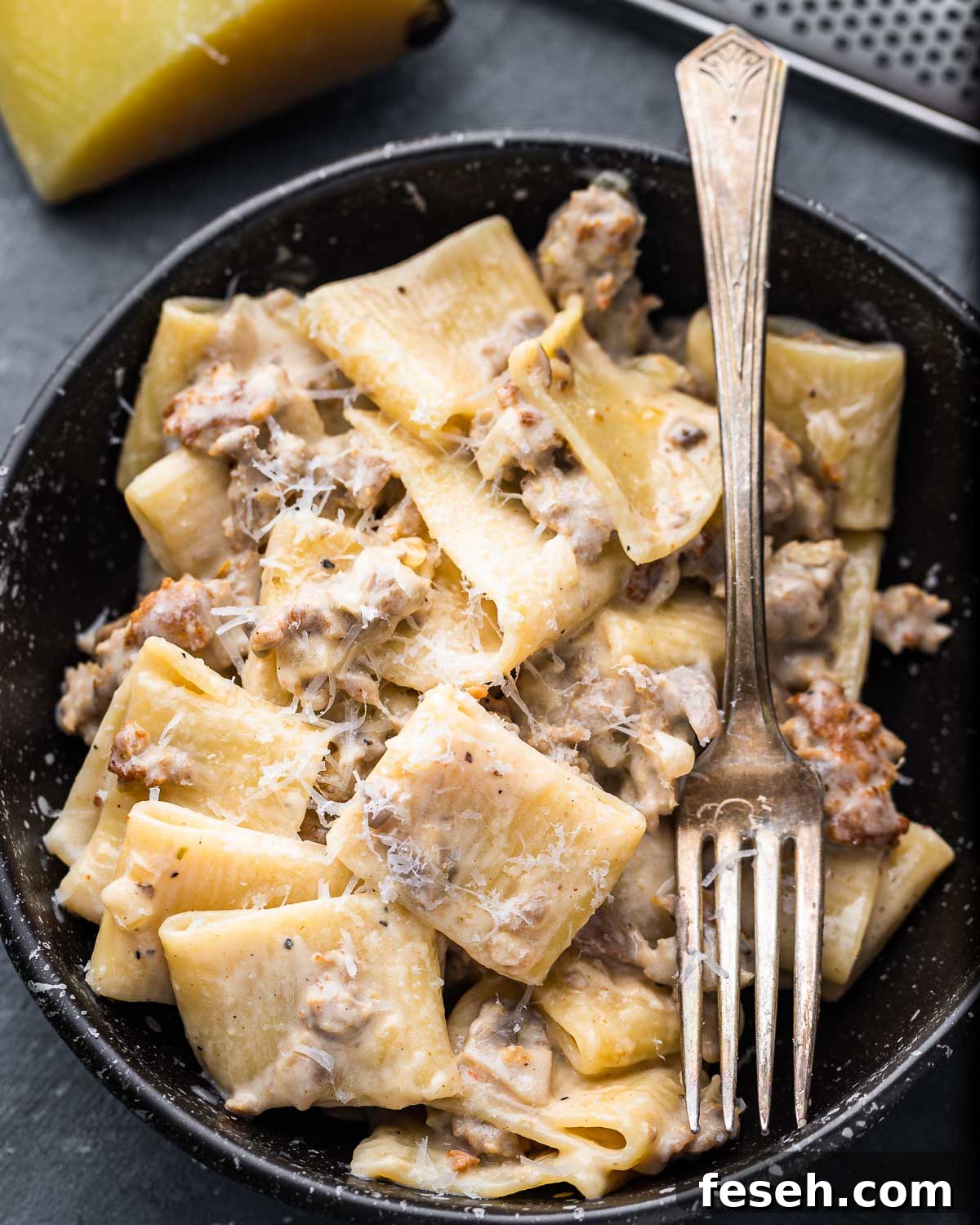 Pasta alla Norcina in black bowl with fork and grated Pecorino on top.