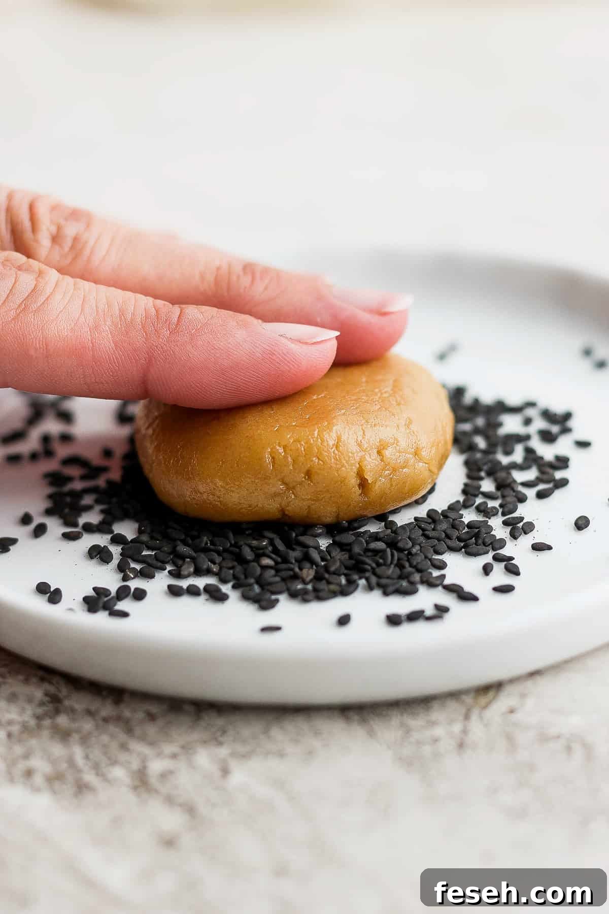 a hand is holding a cookie with sesame seeds on it.