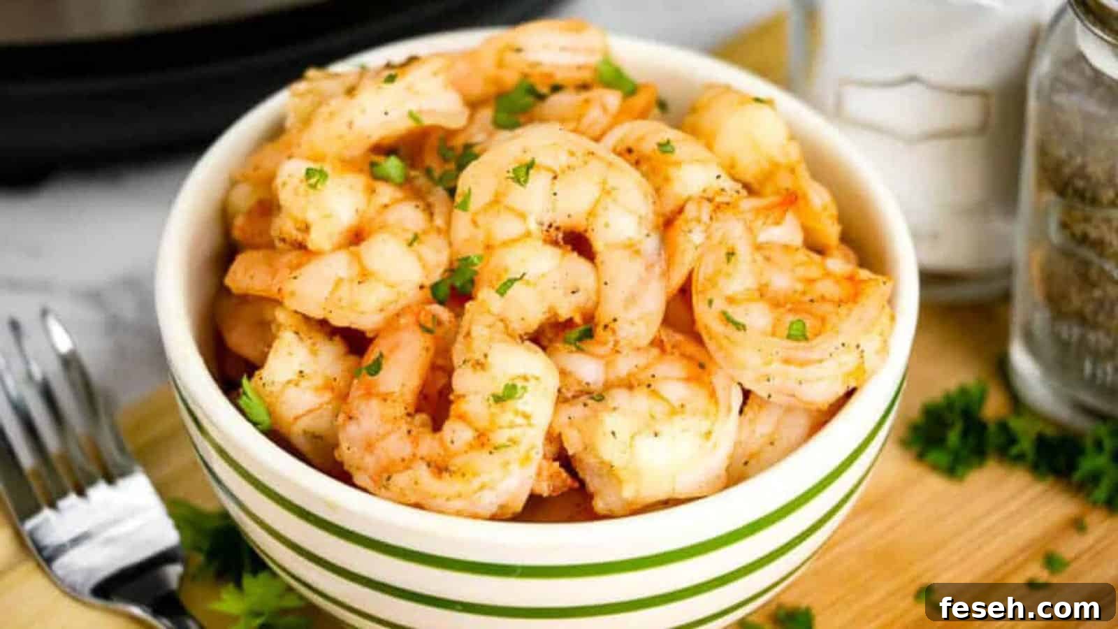 Cooked shrimp in a green and white striped bowl, garnished with parsley.