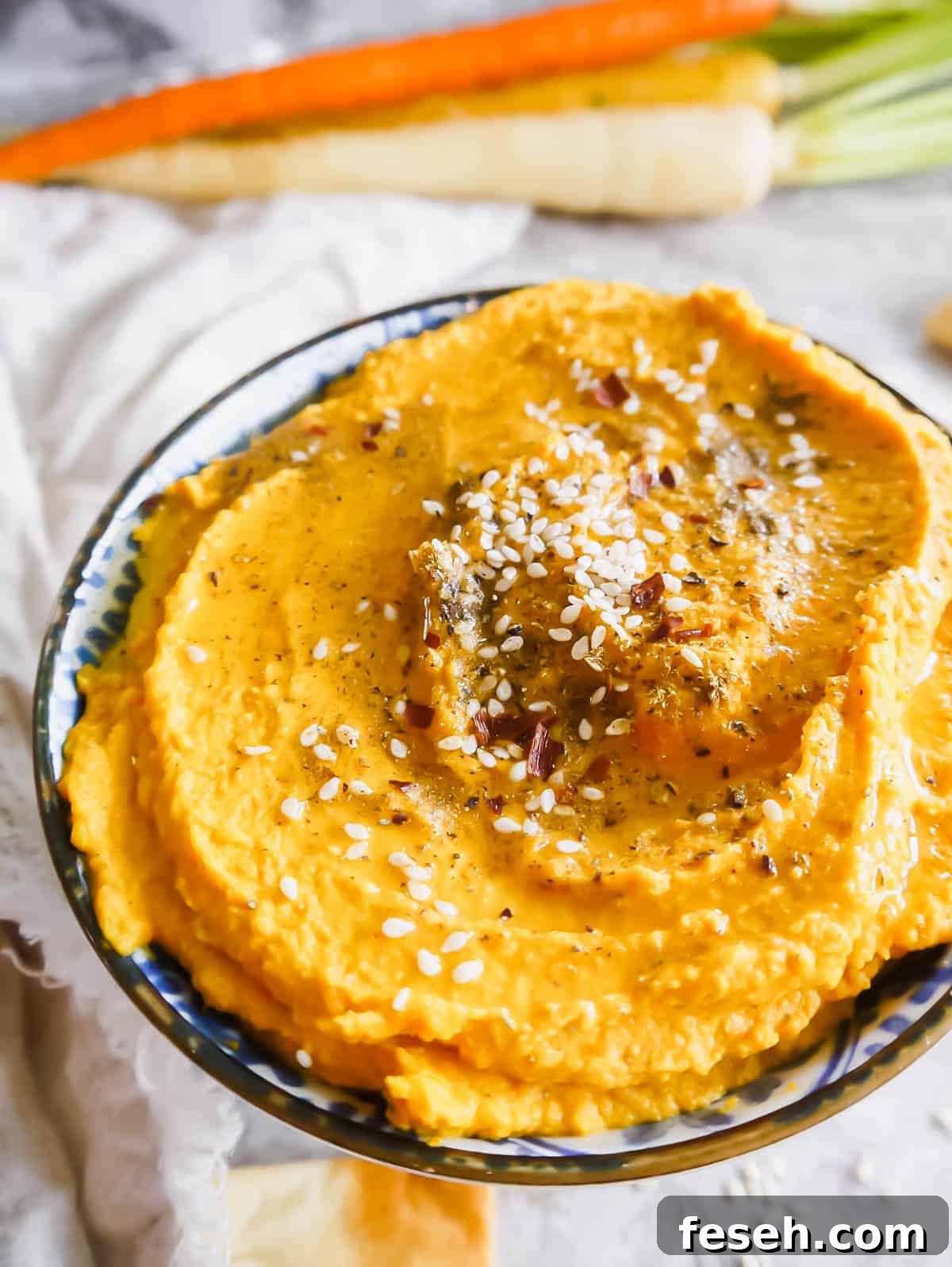 Up close side angle of roasted carrot hummus with sesame seeds, chili flakes and za'atar on top.