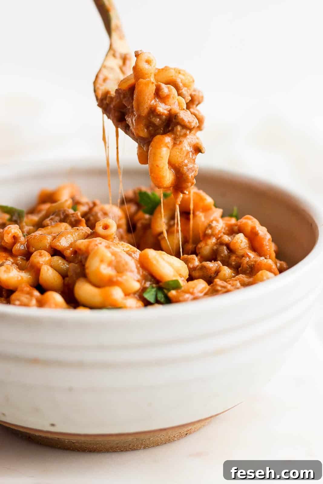 A fork pulling some hamburger helper out of the bowl.