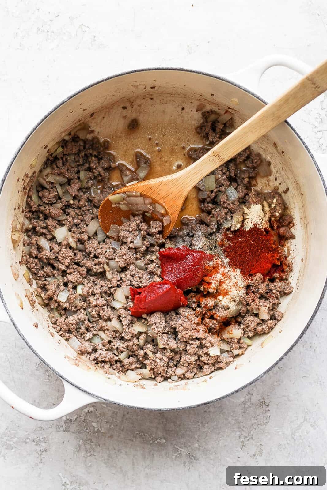 Browned beef in a dutch oven with tomato paste, soy sauce, and seasonings added to the pot.