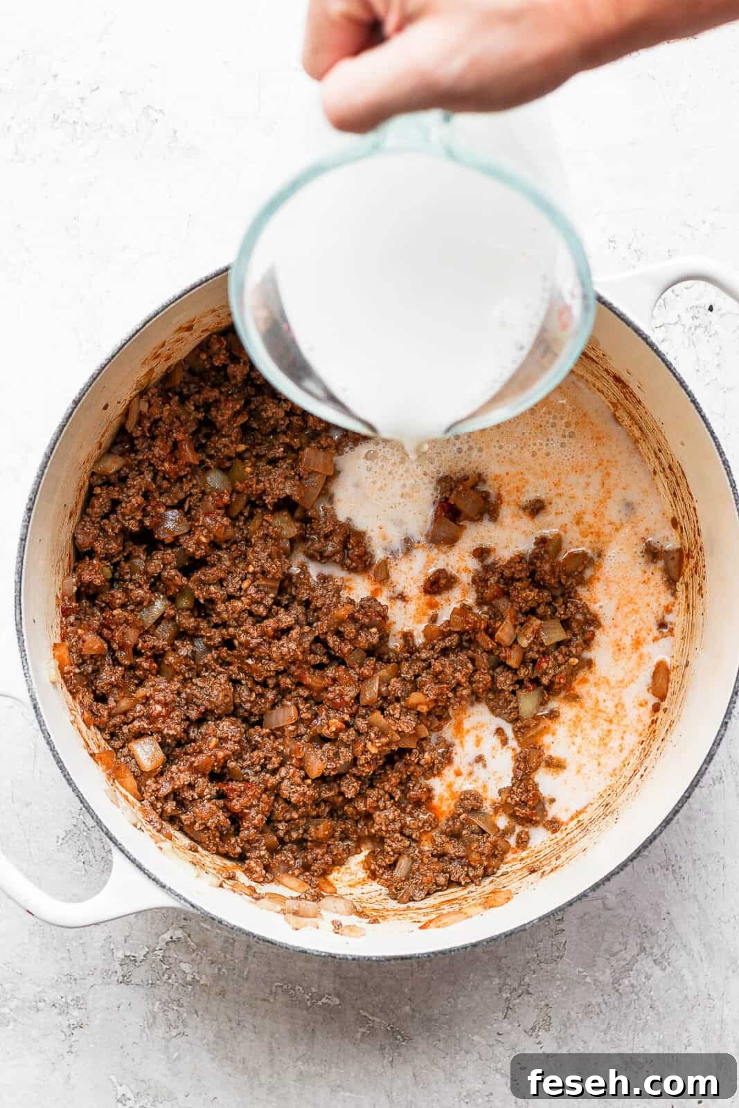Almond milk being poured into the ground beef mixture.