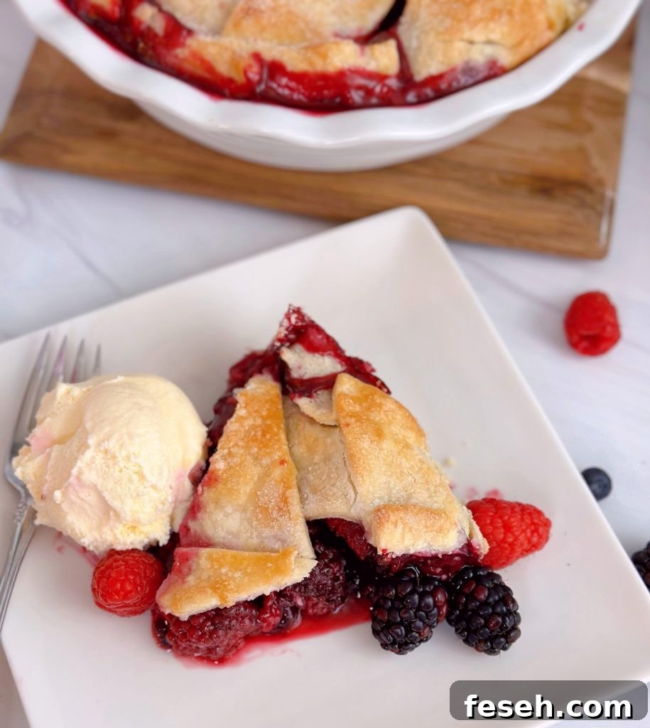 A slice of Triple Berry Deep Dish Galette on a white plate with a scoop of vanilla ice cream.