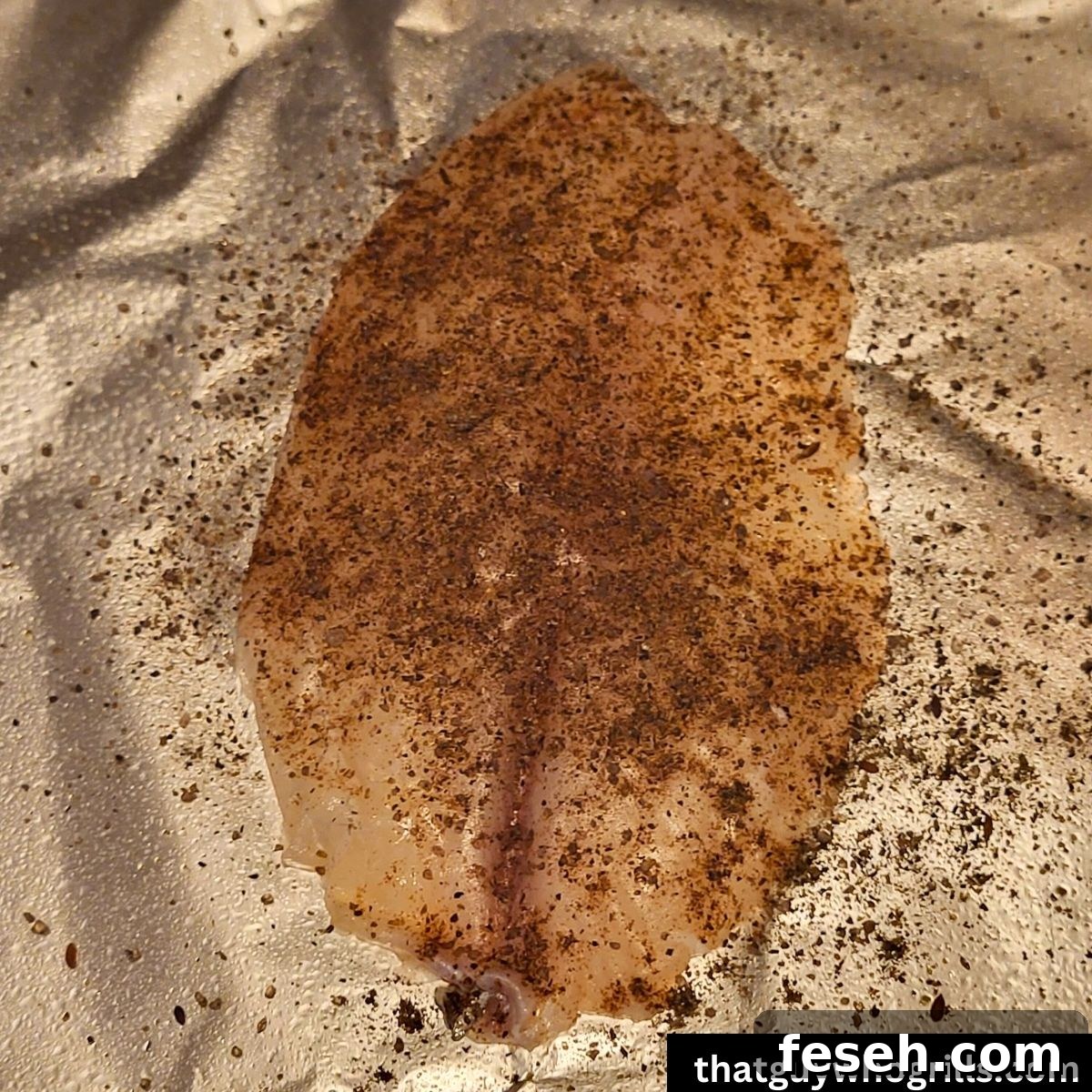 Tilapia filet with blackening seasoning on it laying on tin foil