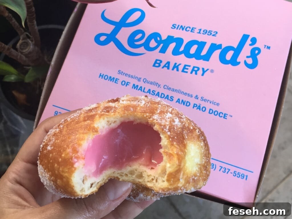 Malasada with pink filling in front of pink box of Leonard's Bakery Malasadas.