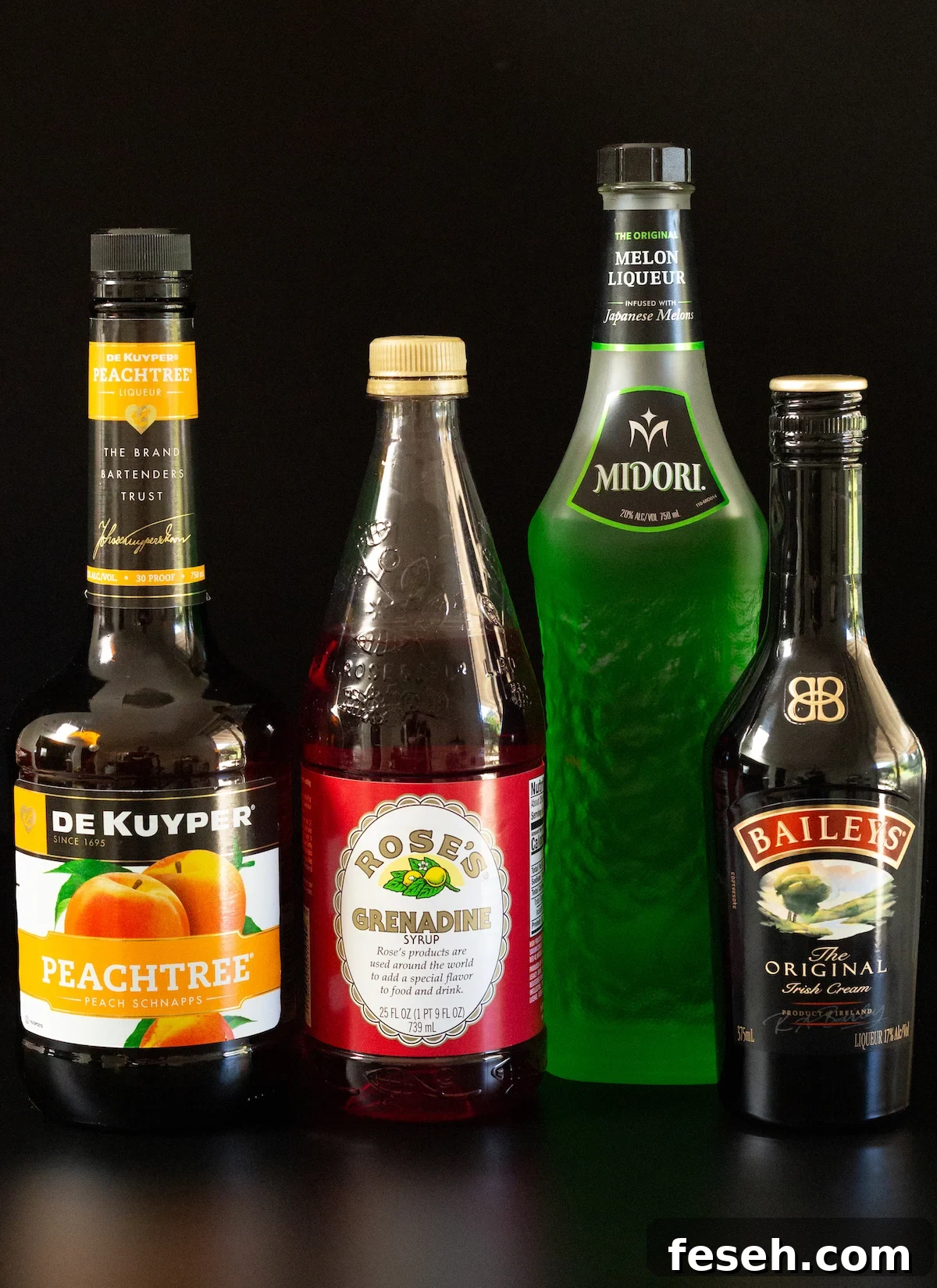 A bottle of peach schnapps, Rose's grenadine, Midori, and Bailey's Irish Cream on a black background.