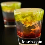 Two shot glasses with the bottom filled with a red liquid, middle is clear, and top is brown and green with the texture of brains.