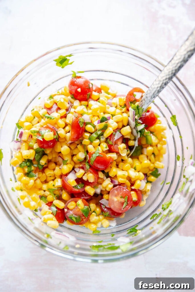 ingredients for tomato corn salsa in a glass bowl with spoon