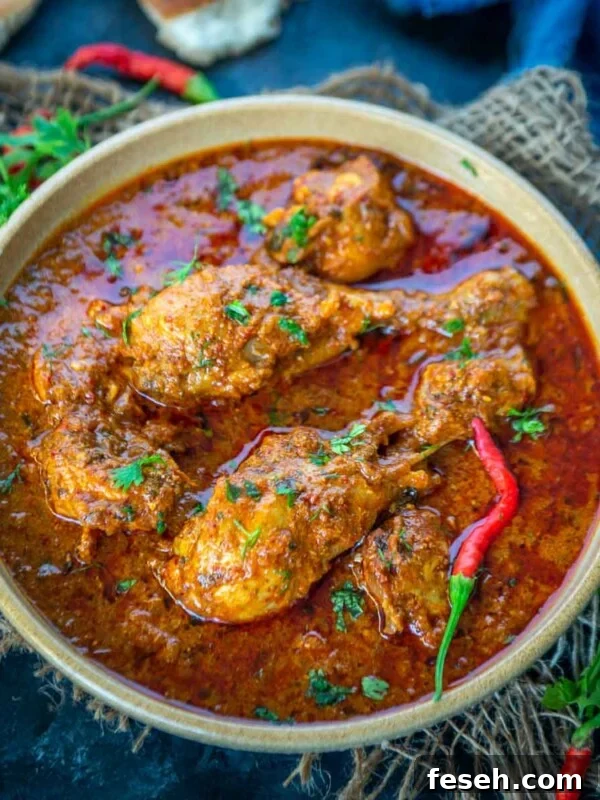 A bowl of spicy Chicken Angara curry garnished with fresh herbs and red chilies.
