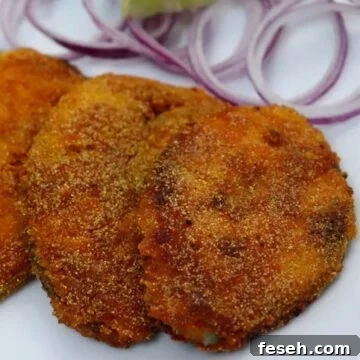 crispy king fish fry goan style served on a white plate with onion rings and lemon wedge.