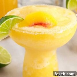close up shot of Peach Margaritas in a glass topped with a slice of lime and peach