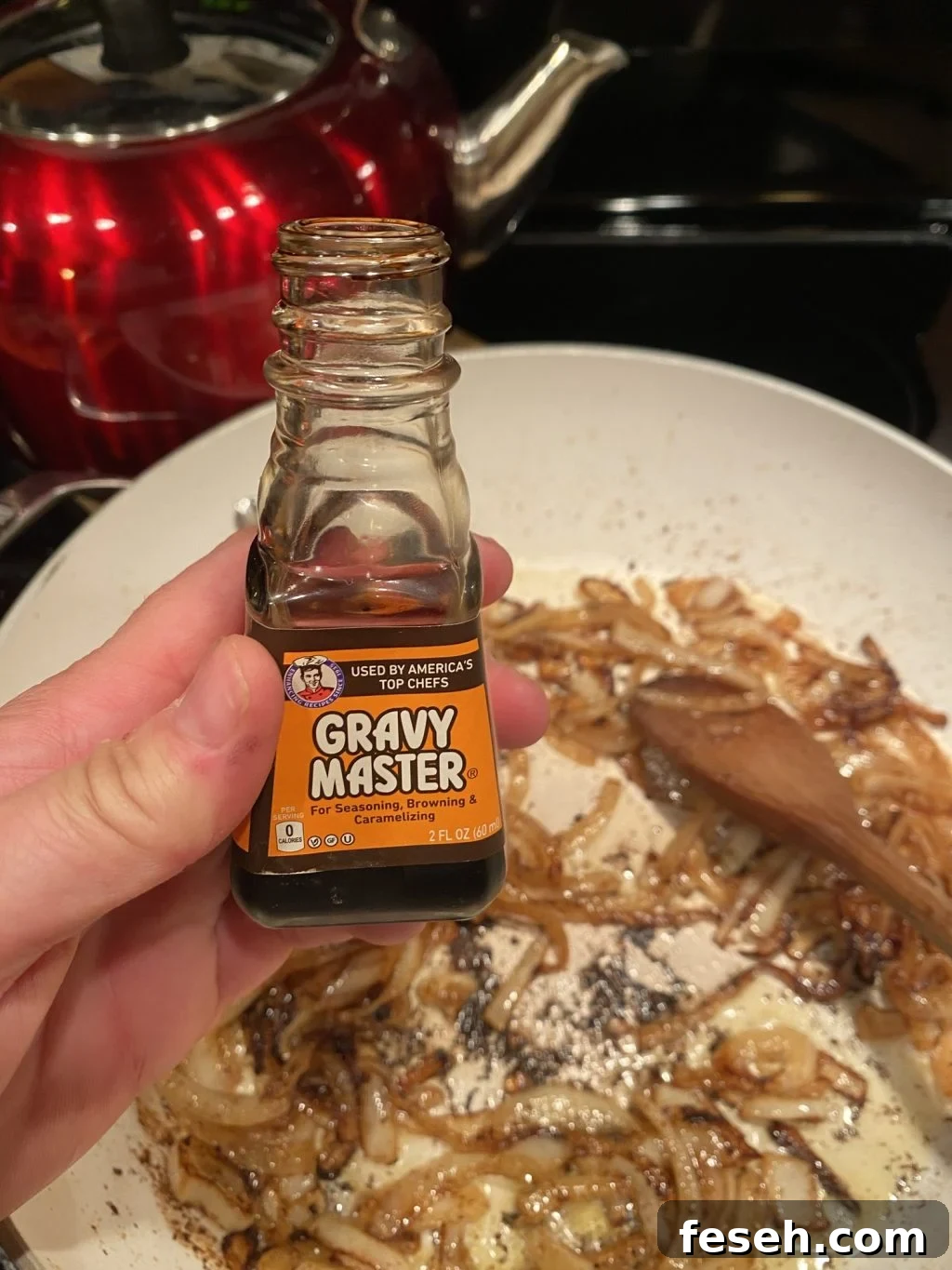 I'm holding a small container of Gravy Master above a pan of sautéing onions