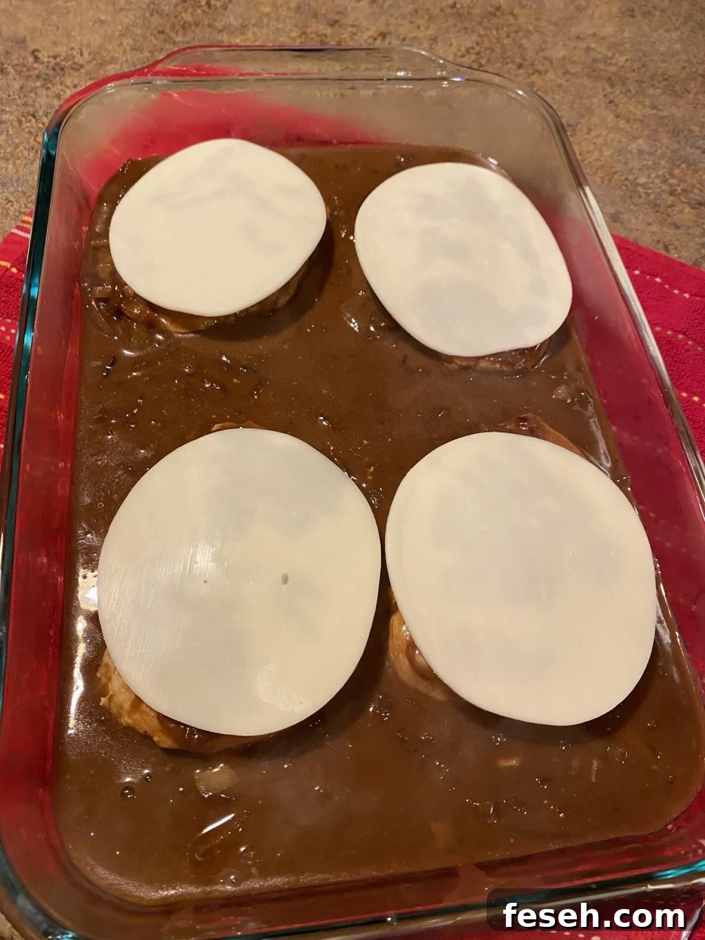 The pork chops are in gravy in the baking dish and each has a slice of cheese placed over it
