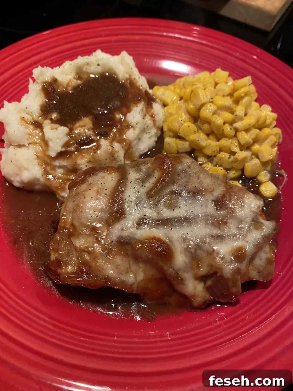 A French Onion Pork Chop on a plate with gravy, mashed potatoes, and corn