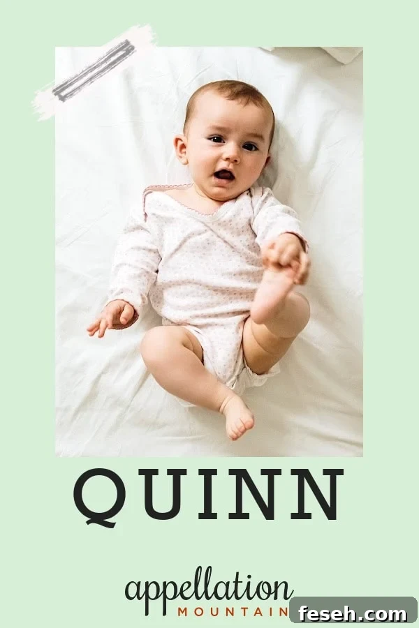 baby lying on back, holding one foot, wearing light yellow snapsuit; baby name Quinn