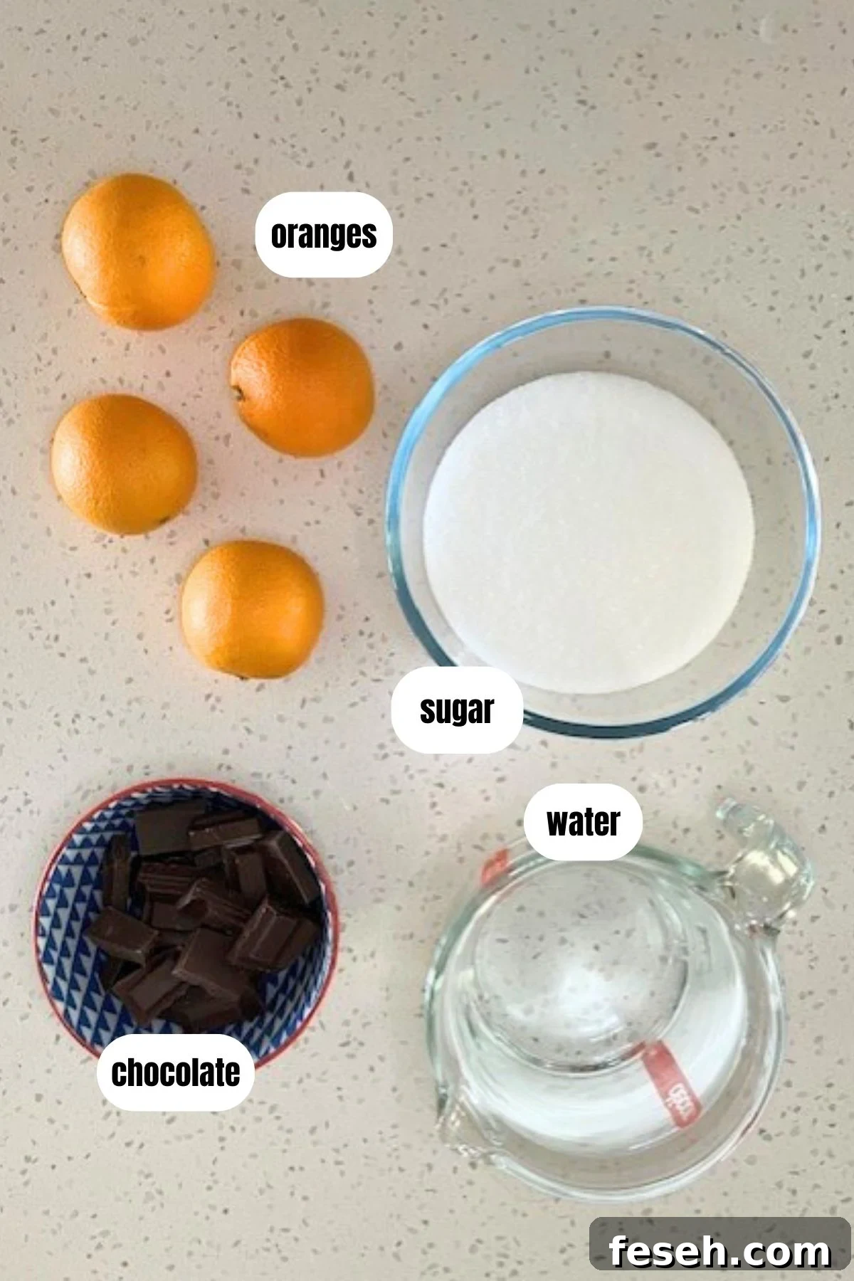 Labelled overhead of ingredients for candied orange slices dipped in chocolate, including oranges, water, sugar and chocolate.