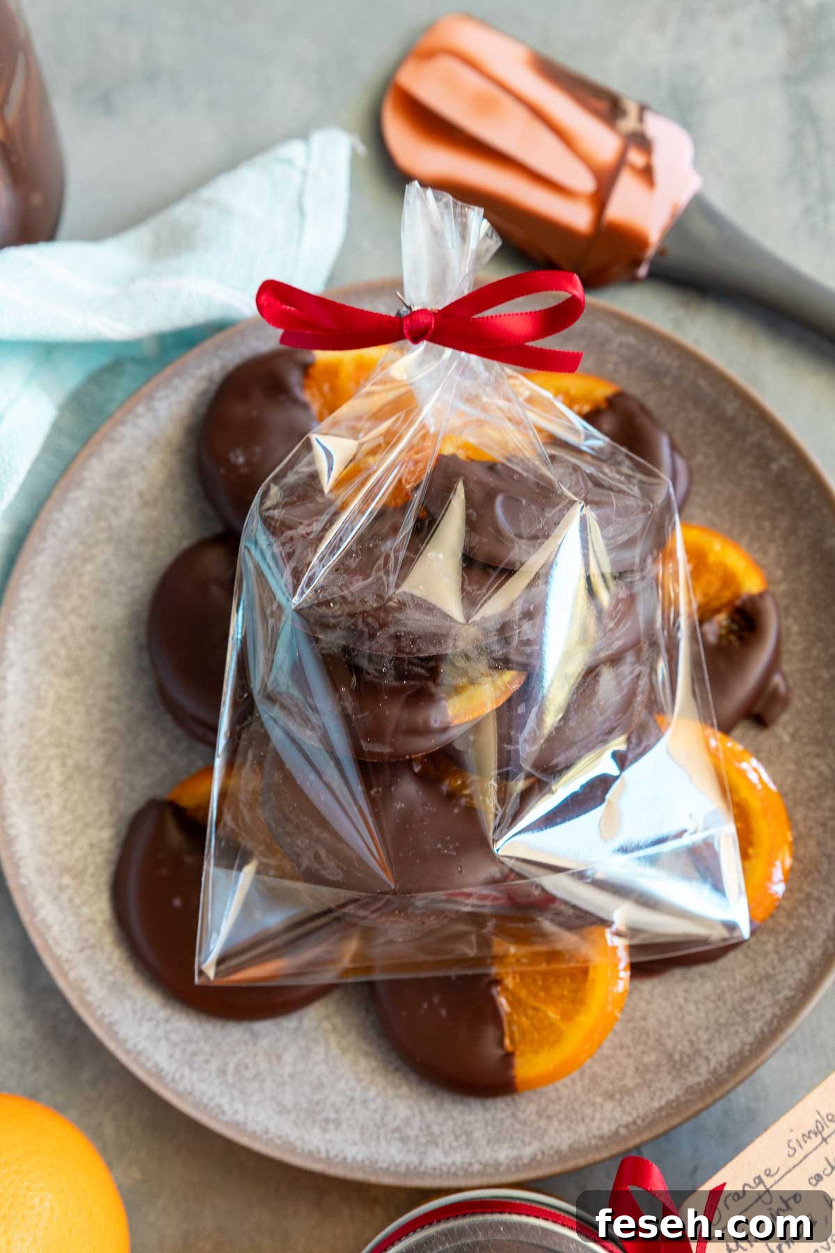 A small see-through gift bag with candied oranges dipped in chocolate in it, on a blue plate of more orange slices.