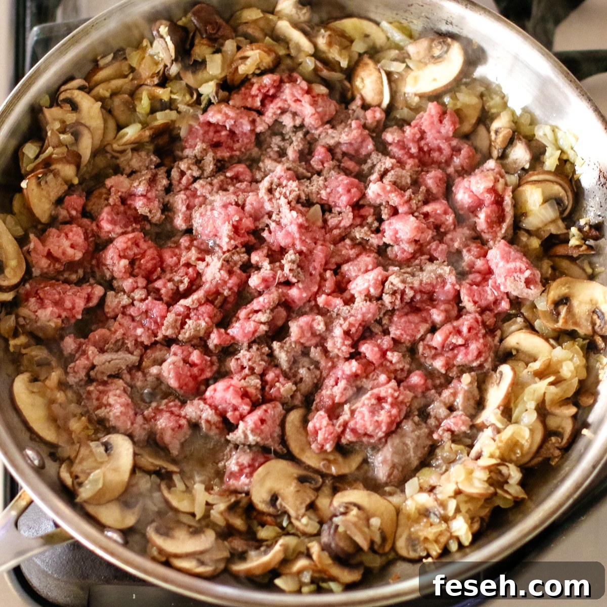 cooking beef and mushrooms in a stainless steel pan.