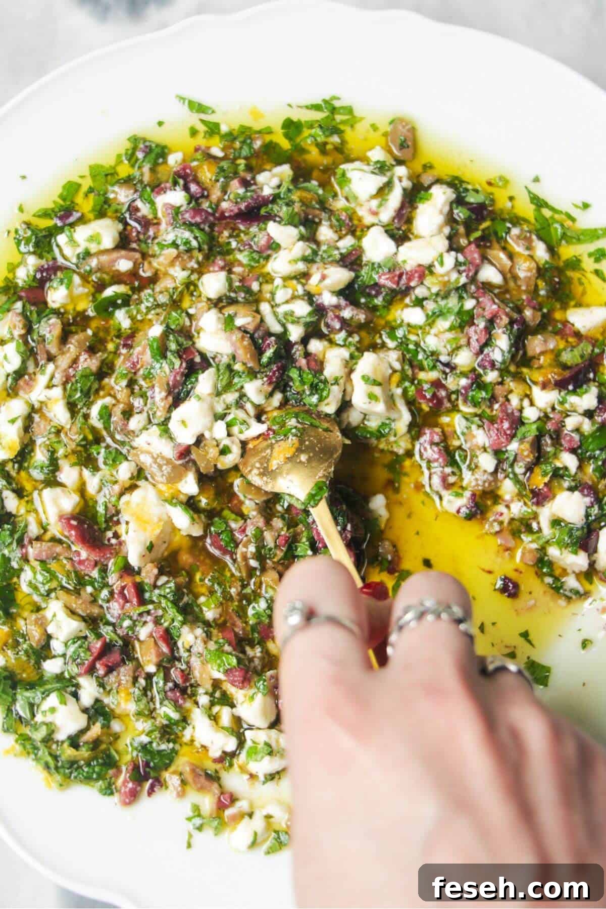 Hand mixing ingredients for Greek dipping oil in a large white plate.
