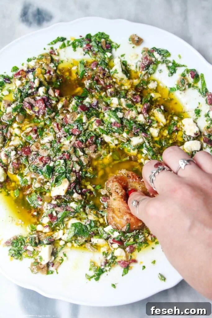 Hand swirling bread through Greek dipping oil in a large white plate.