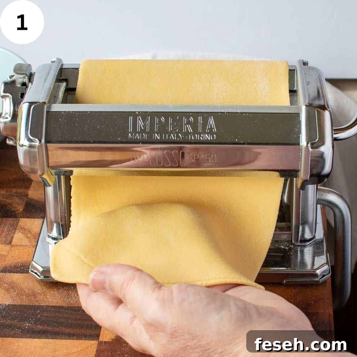Pasta dough being rolled through a hand cranked pasta machine.