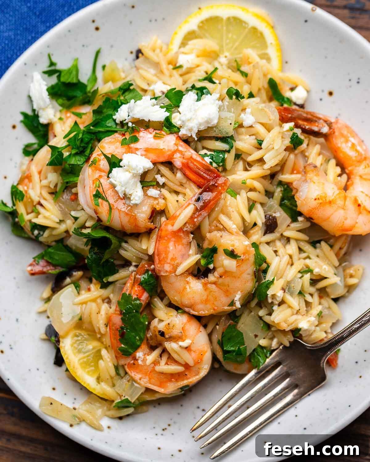 White plate with orzo topped with shrimp and parsley.