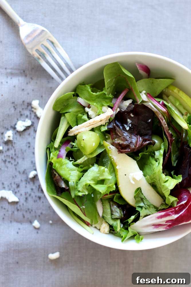 White bowl containing a Pear and Goat Cheese Bistro Salad, fork on table.