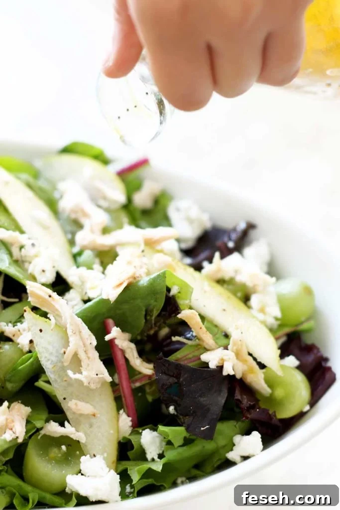 Hand pouring in a mango vinaigrette onto a bowl of containing Pear and Goat Cheese Bistro Salad.