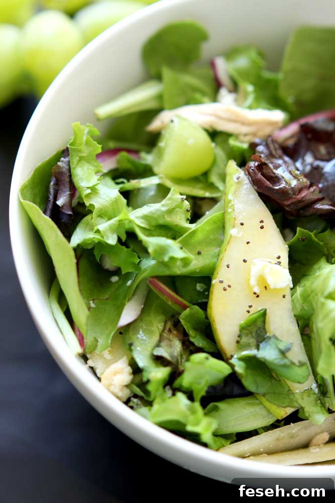 White bowl containing a Pear and Goat Cheese Bistro Salad, topped with pear and poppy seeds.
