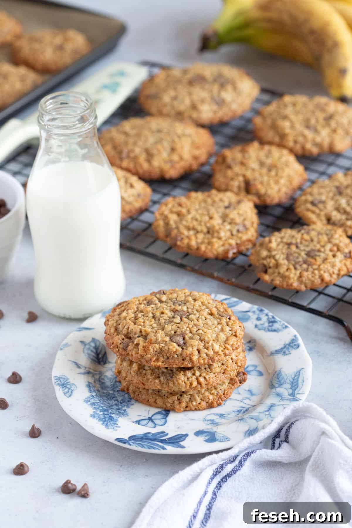 A stack of banana oat cookies on a blue and white plate, with a glass of milk.
